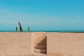 Una escalera de hormigón conduce a un balcón con vistas a un cielo azul despejado y un mar tranquilo.