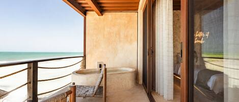 Un balcón con vista a la playa, techo de madera, una bañera y una cama con vistas.