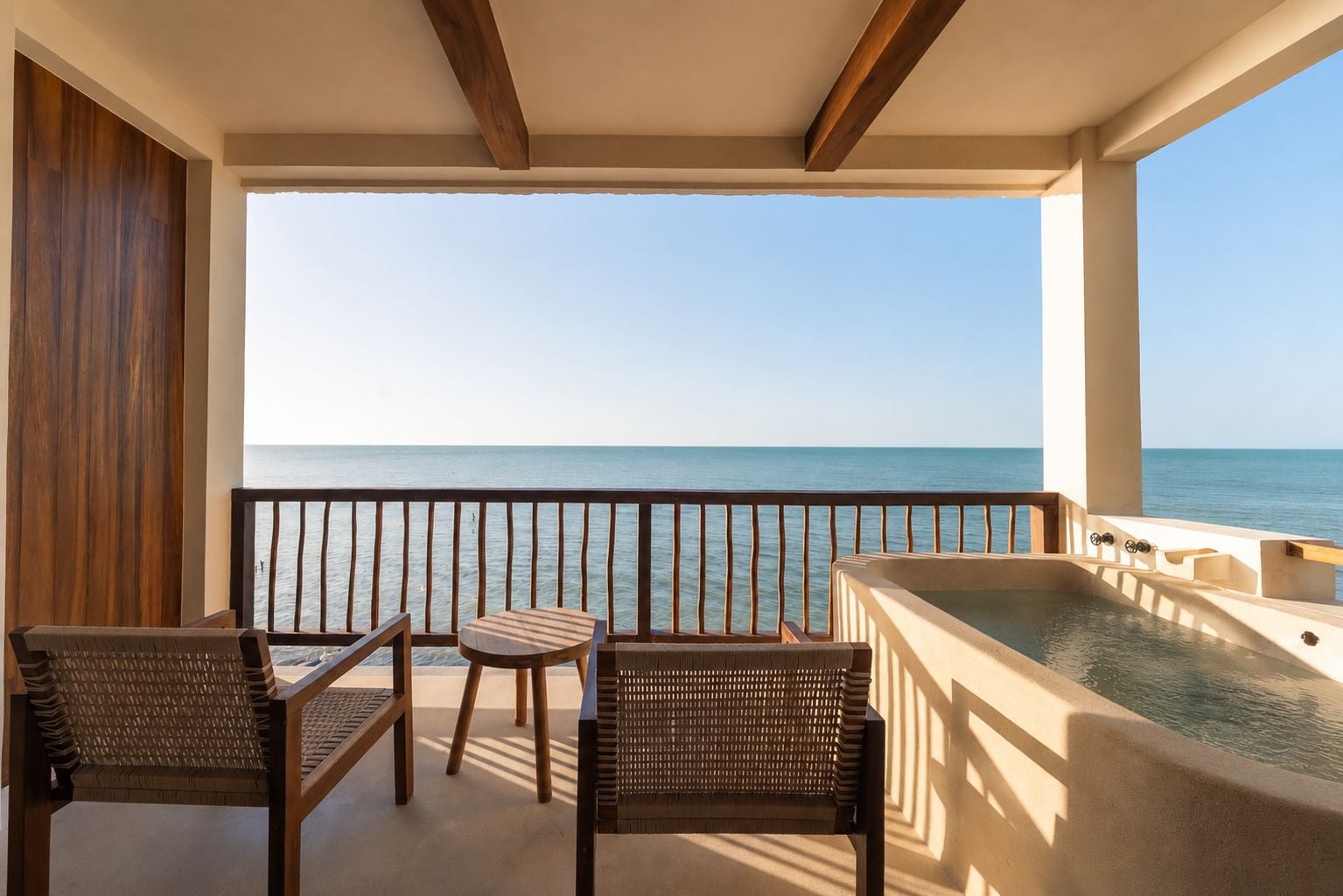 A balcony with a view of the sea, a hot tub, and wicker furniture.