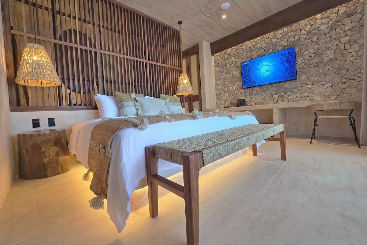 A modern bedroom with a bed, bedside lamps, a stone wall, a television, and a desk.