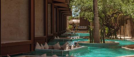 A series of rectangular water features with seating, surrounded by a wooden structure and palm trees.