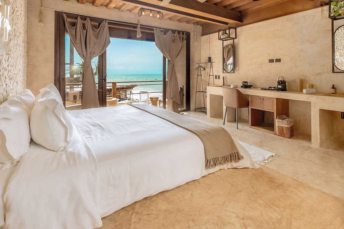 A bedroom with a large bed, a desk, and a view of the sea.