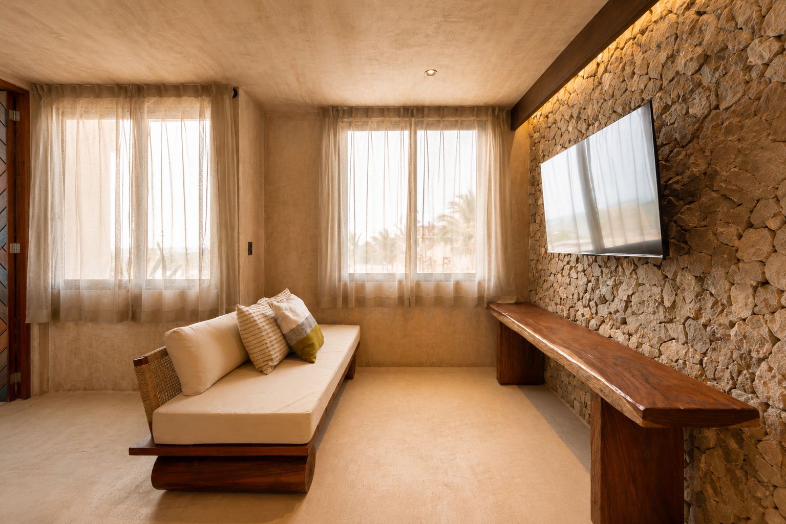 Una habitación con un sofá, un banco de madera, una pared de piedra y un televisor montado.