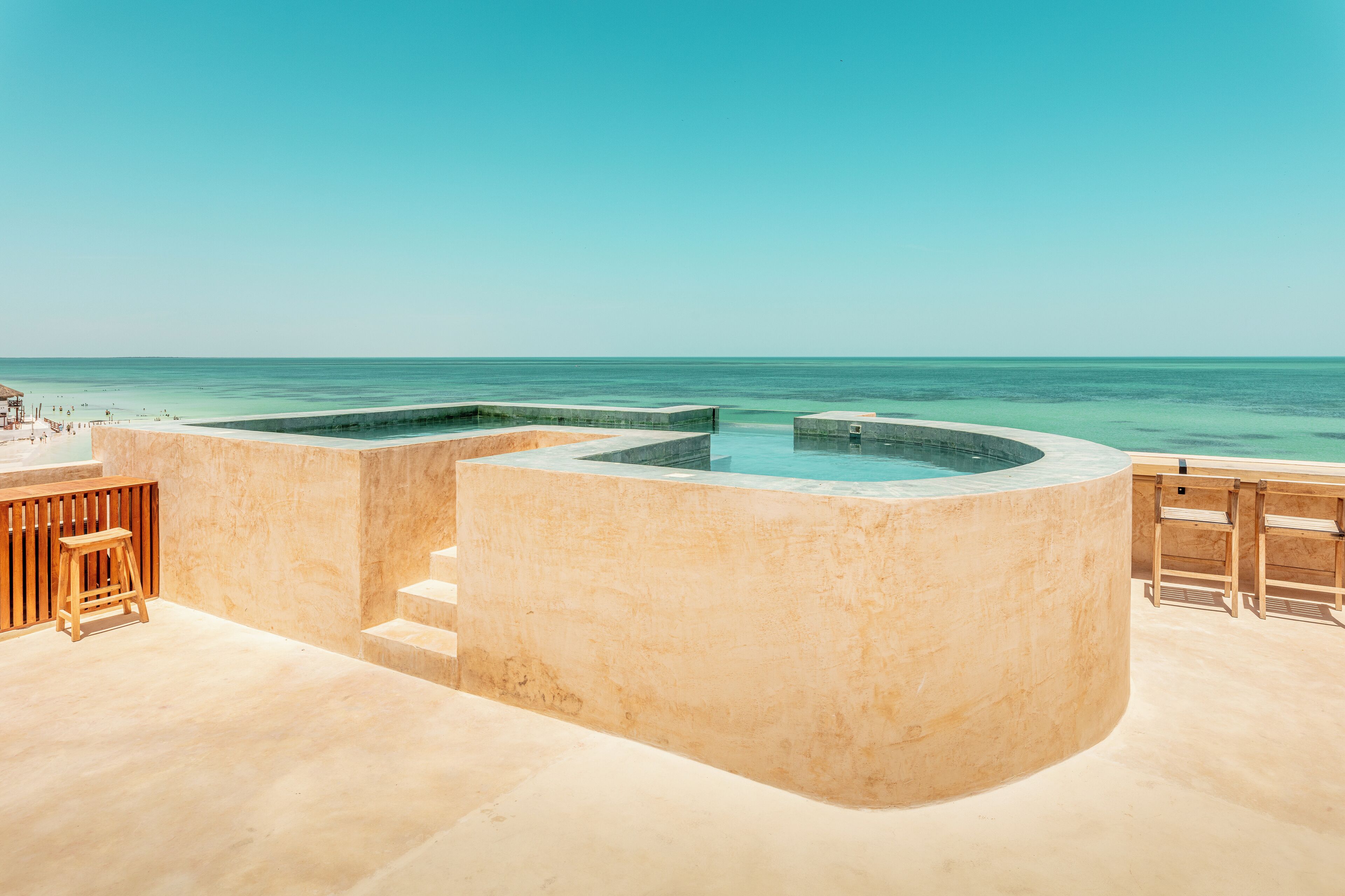Un espace piscine avec vue sur l’océan, une terrasse en bois et une structure en béton.