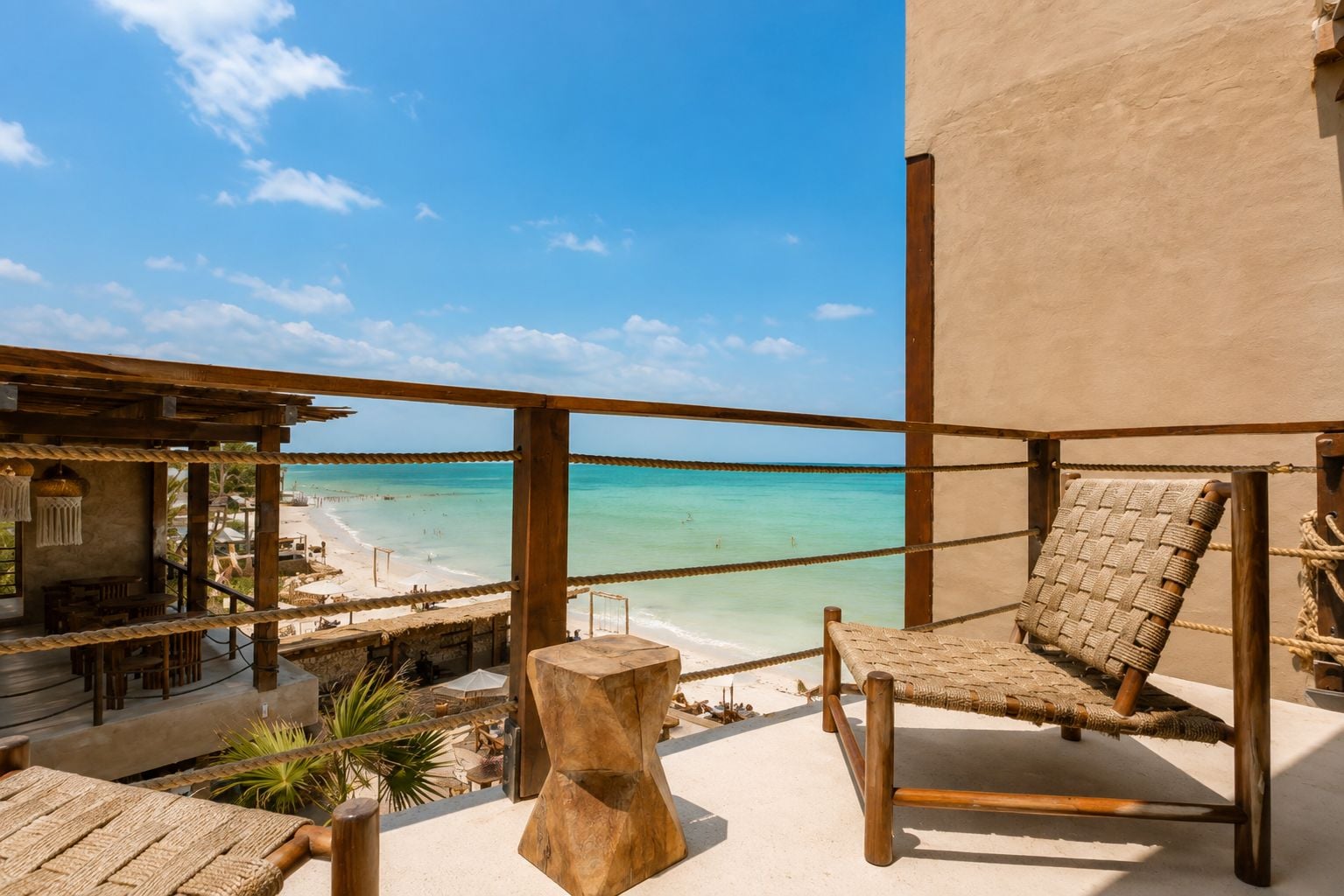 A beachside balcony with a view of the ocean, a woven chair, and a rustic wooden table.