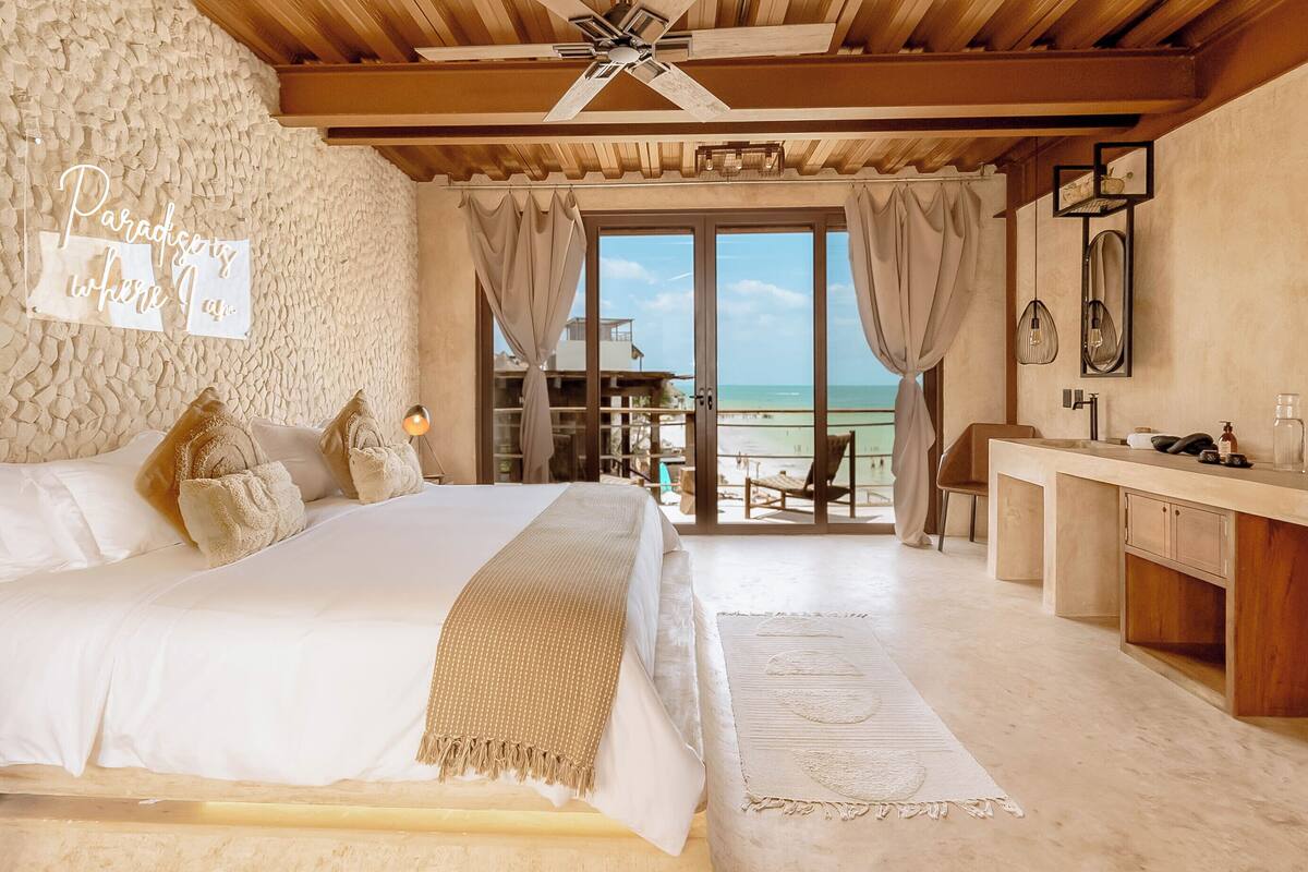 A bedroom with a bed, a desk, and a view of the ocean.