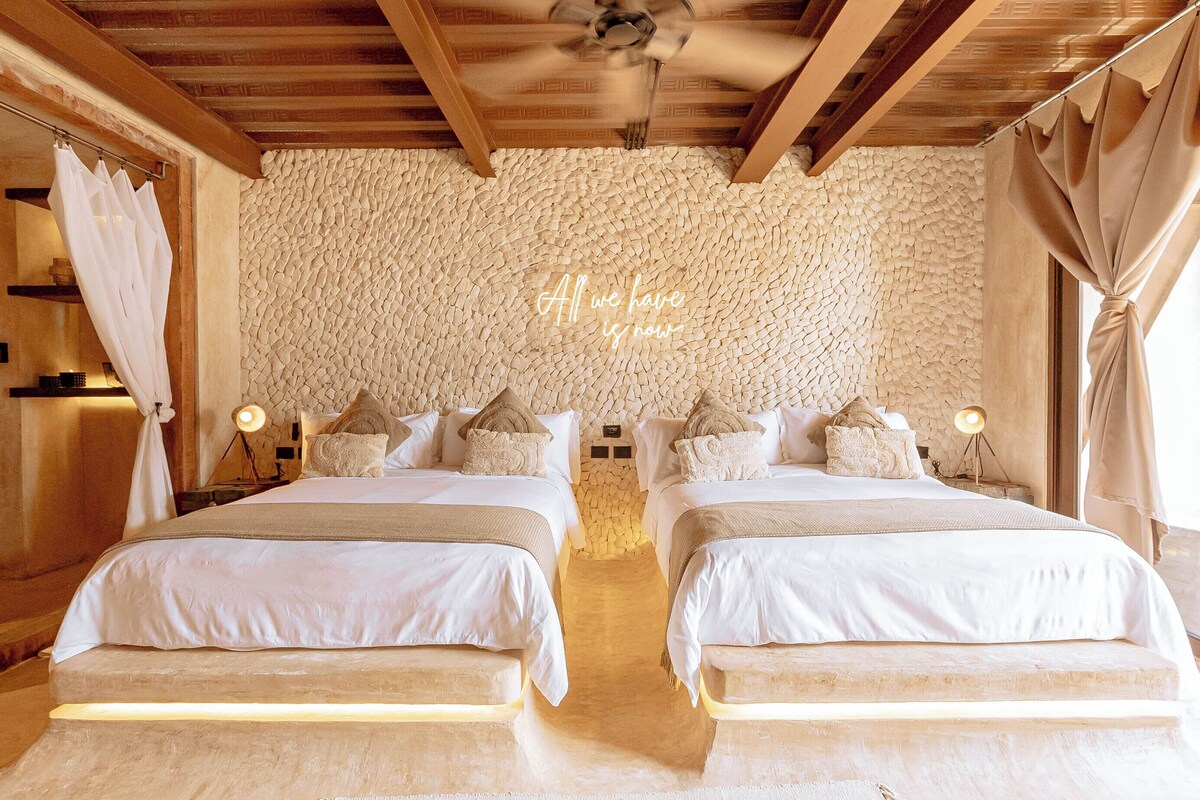 Una cama doble con una pared de piedra al fondo y un ventilador de techo arriba.