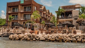 Un complejo turístico con varias construcciones, zonas de estar al aire libre y un litoral rocoso.