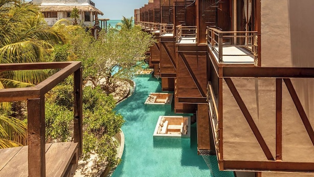 Un resort con bungalows sobre el agua, piscina y exuberante vegetación tropical.
