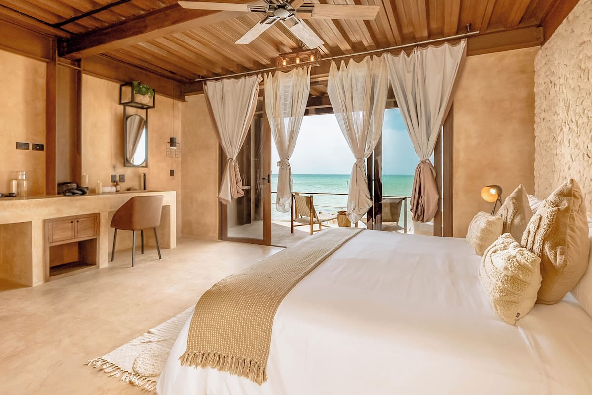 A bedroom with a bed, a desk, and a chair, with a view of the ocean.