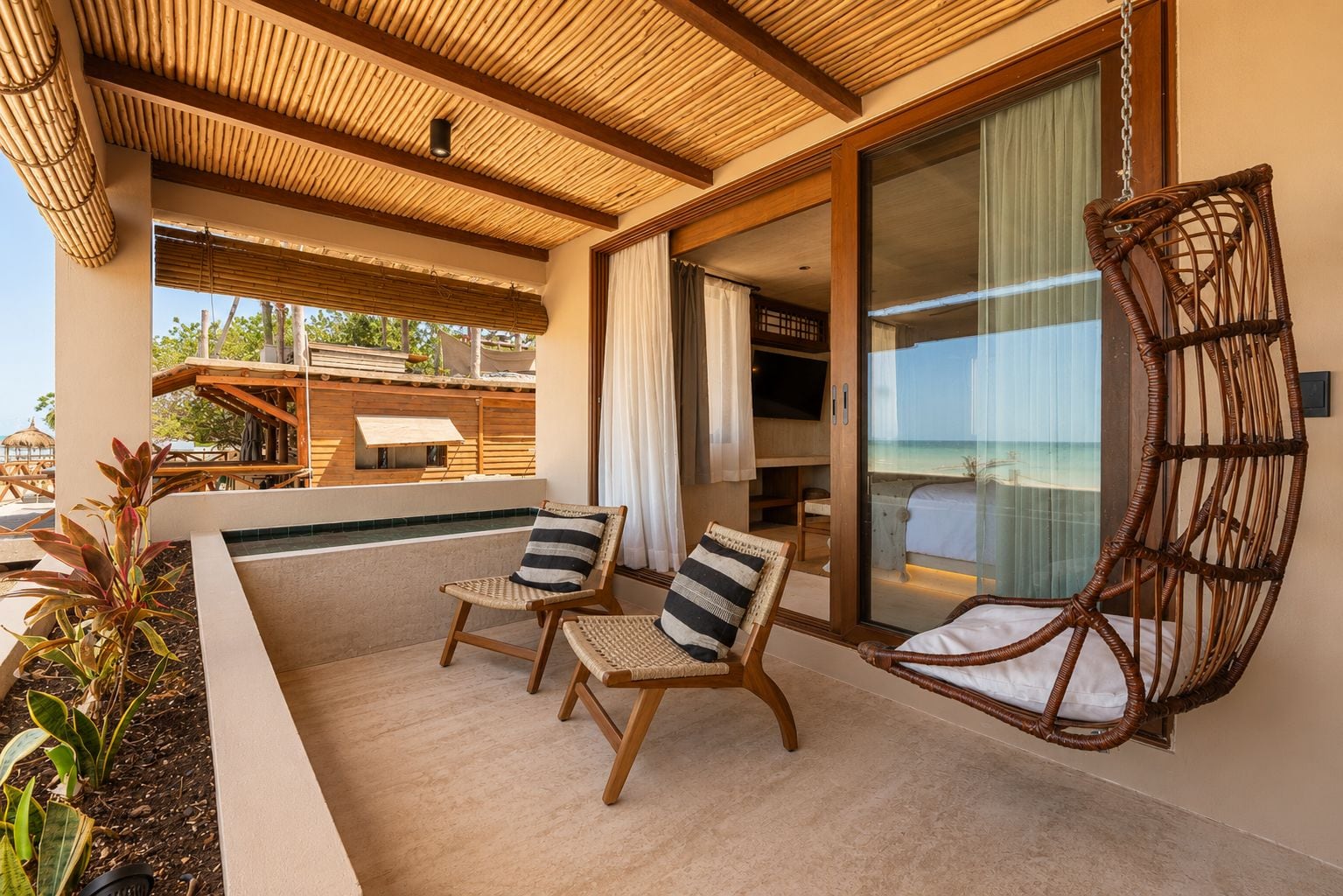 A balcony with two wicker chairs, a view of the ocean, and a sliding glass door leading to a bedroom.