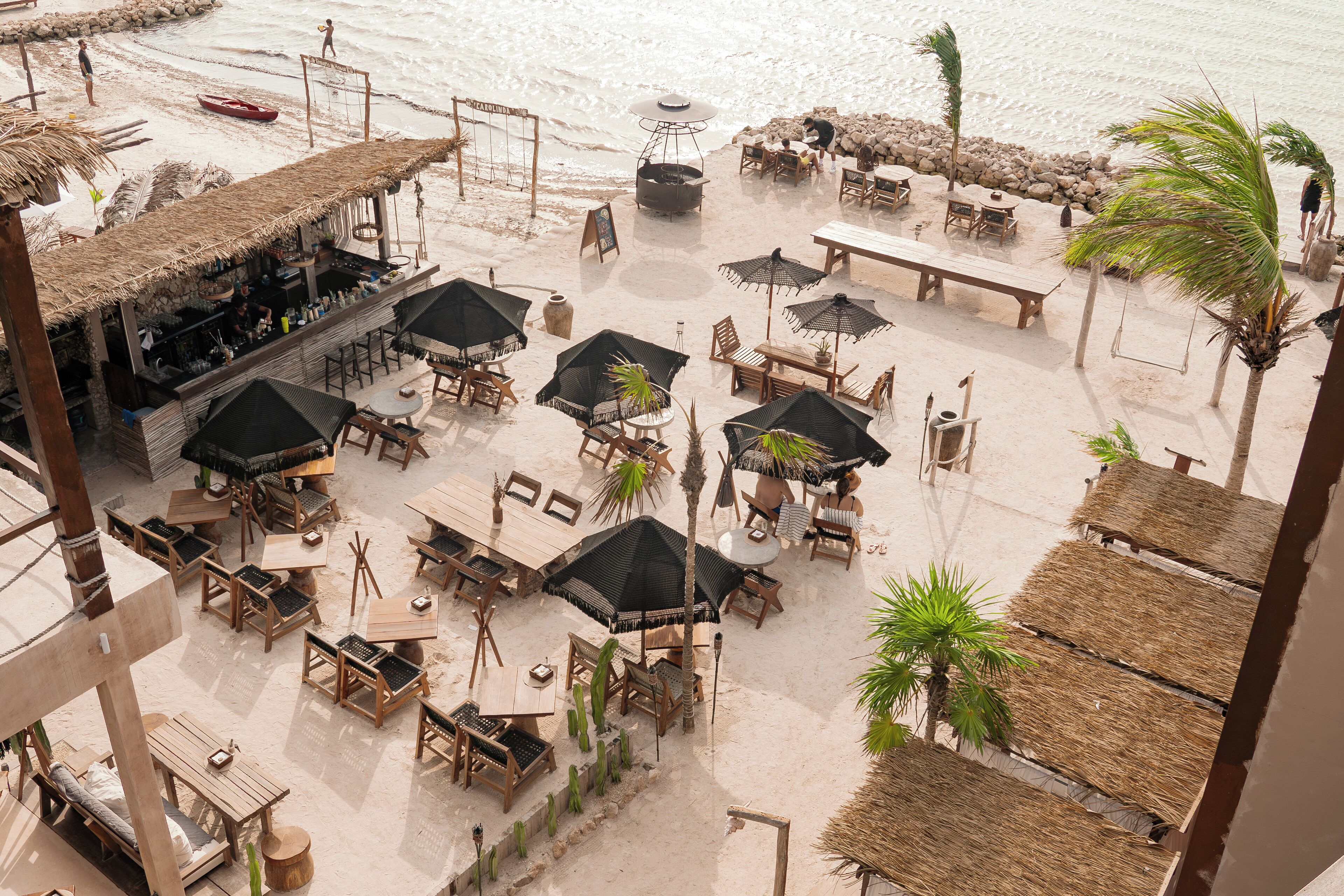 A beachside restaurant with outdoor seating, including tables and chairs, and a bar area.