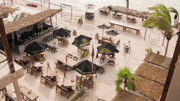 A beachside restaurant with outdoor seating, including tables and chairs, and a bar area.