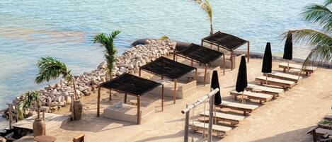A beachside lounge with wooden tables and chairs, a stone wall, and umbrellas.