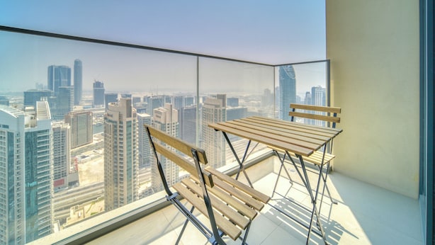 Een balkon met twee houten stoelen en een tafel, met uitzicht op een stadsgezicht met hoge gebouwen.