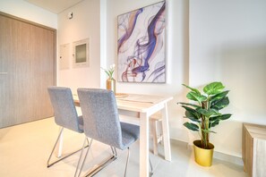 Un comedor moderno con una mesa blanca y dos sillas grises, un cuadro abstracto grande en la pared y una planta en maceta.
