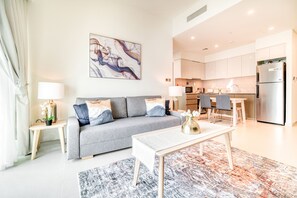A modern living room with a grey sofa, a coffee table, and a patterned rug. A kitchen is visible in the background with white cabinets and stainless steel appliances. - City Lights and Luxury Living, Close to Dubai Mall (Dubai)