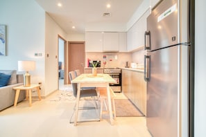 A modern kitchen with stainless steel appliances, a dining area with a table and chairs, and a living area with a sofa and lamp. - City Lights and Luxury Living, Close to Dubai Mall (Dubai)