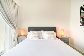 Una cama bien hecha con sábanas blancas y dos lámparas de noche a cada lado.