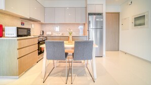 A modern kitchen with white cabinets, a stainless steel refrigerator, a microwave, and a stove. There are two grey chairs around a small table with a vase of flowers.