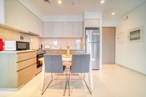 Una cocina moderna con armarios blancos, un refrigerador de acero inoxidable, un microondas y una estufa. Hay dos sillas grises alrededor de una mesa pequeña con un florero.