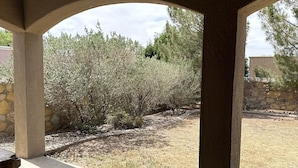 A covered patio area with a view of a landscaped garden and a stone wall. - Entire Cozy Home in West El Paso (El Paso)