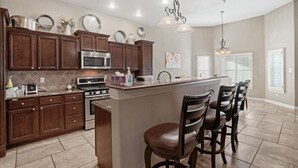 A modern kitchen with dark wood cabinets, stainless steel appliances, and a central island with bar stools. - Entire Cozy Home in West El Paso (El Paso)