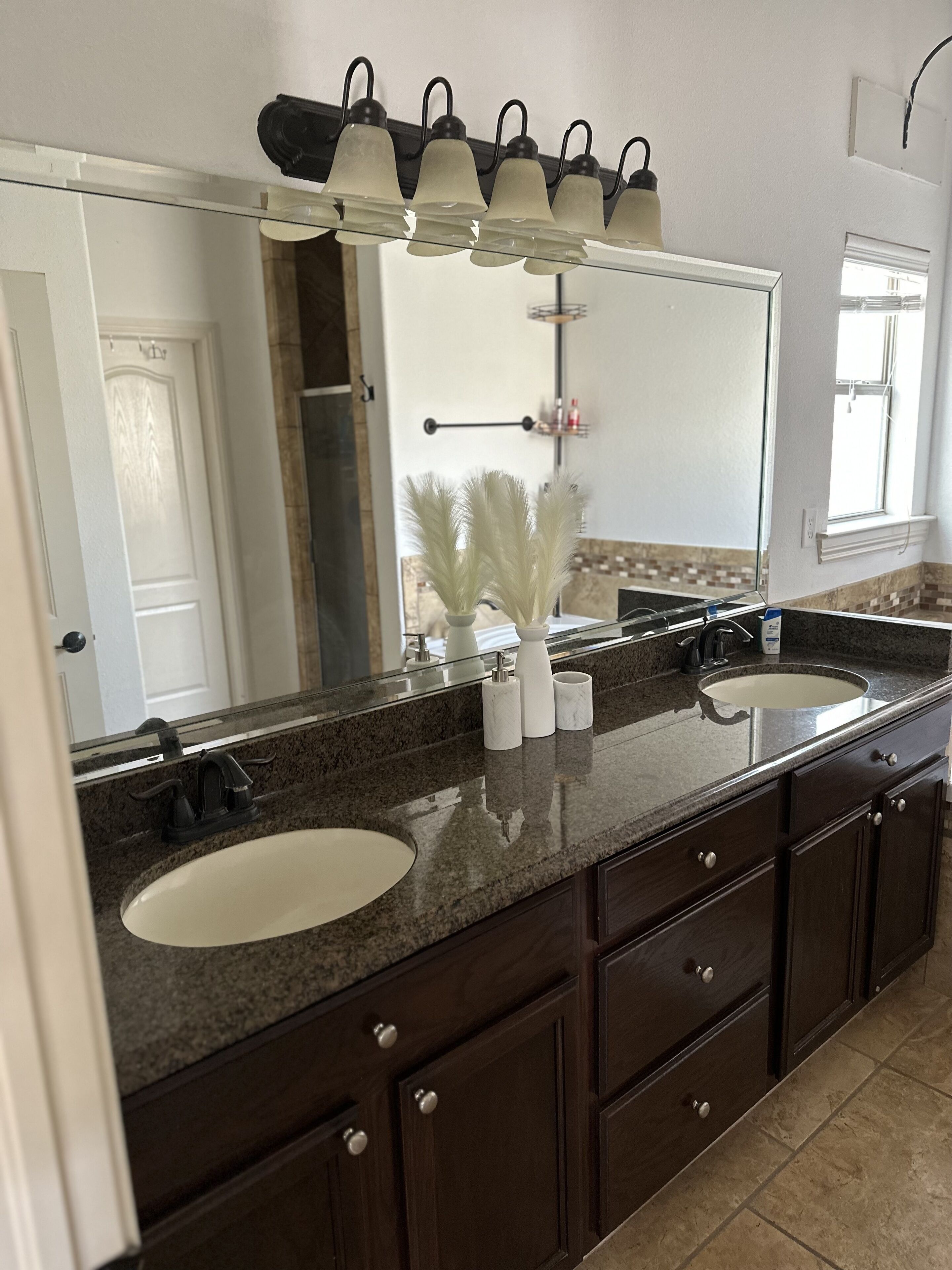 Un bagno con due lavabi, mobili in legno scuro, uno specchio grande e un lampadario sopra lo specchio.