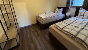 A hotel room with two beds, a wooden floor, a metal shelf unit, and a window with curtains. - Ferienwohnung Berger (Penig)