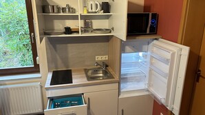 A compact kitchen with a built-in microwave, a small sink, and a refrigerator. - Ferienwohnung Berger (Penig)