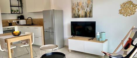 A modern kitchen with white cabinets, a stainless steel refrigerator, a microwave, and a dining area with a table and chairs.
