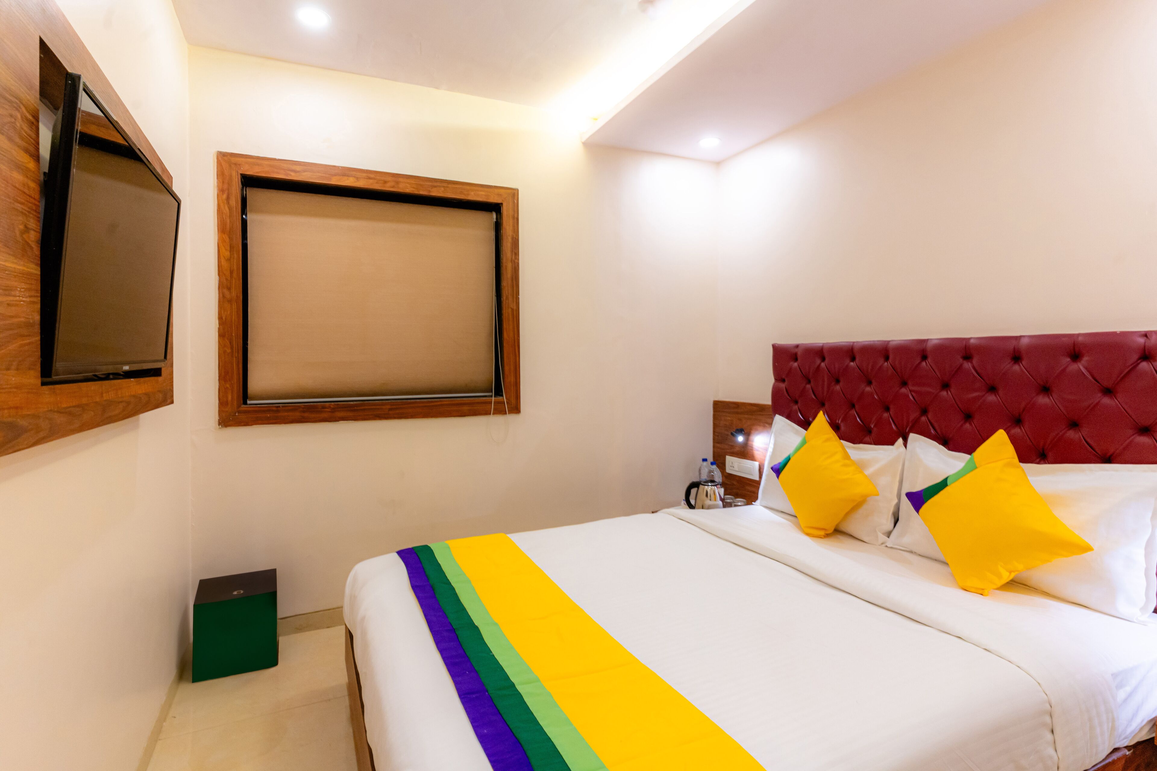 A hotel room with a bed, a television mounted on the wall, and a bedside table with a lamp.