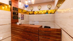A hotel reception area with a wooden reception desk, multiple clocks on the wall, and a check-in sign. - Itsy Hotels Elegant (Mumbai)