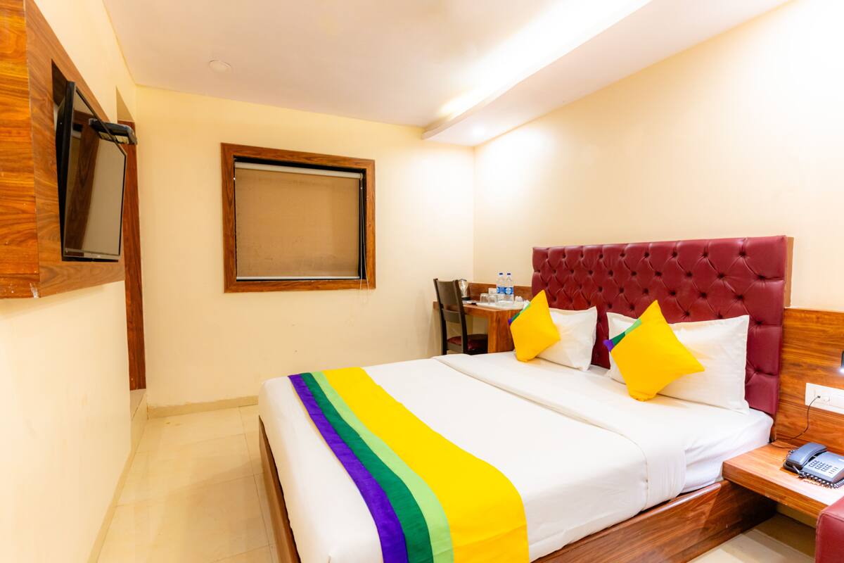 A hotel room with a large bed, a wooden headboard, a bedside table with a phone, and a window with a wooden frame.