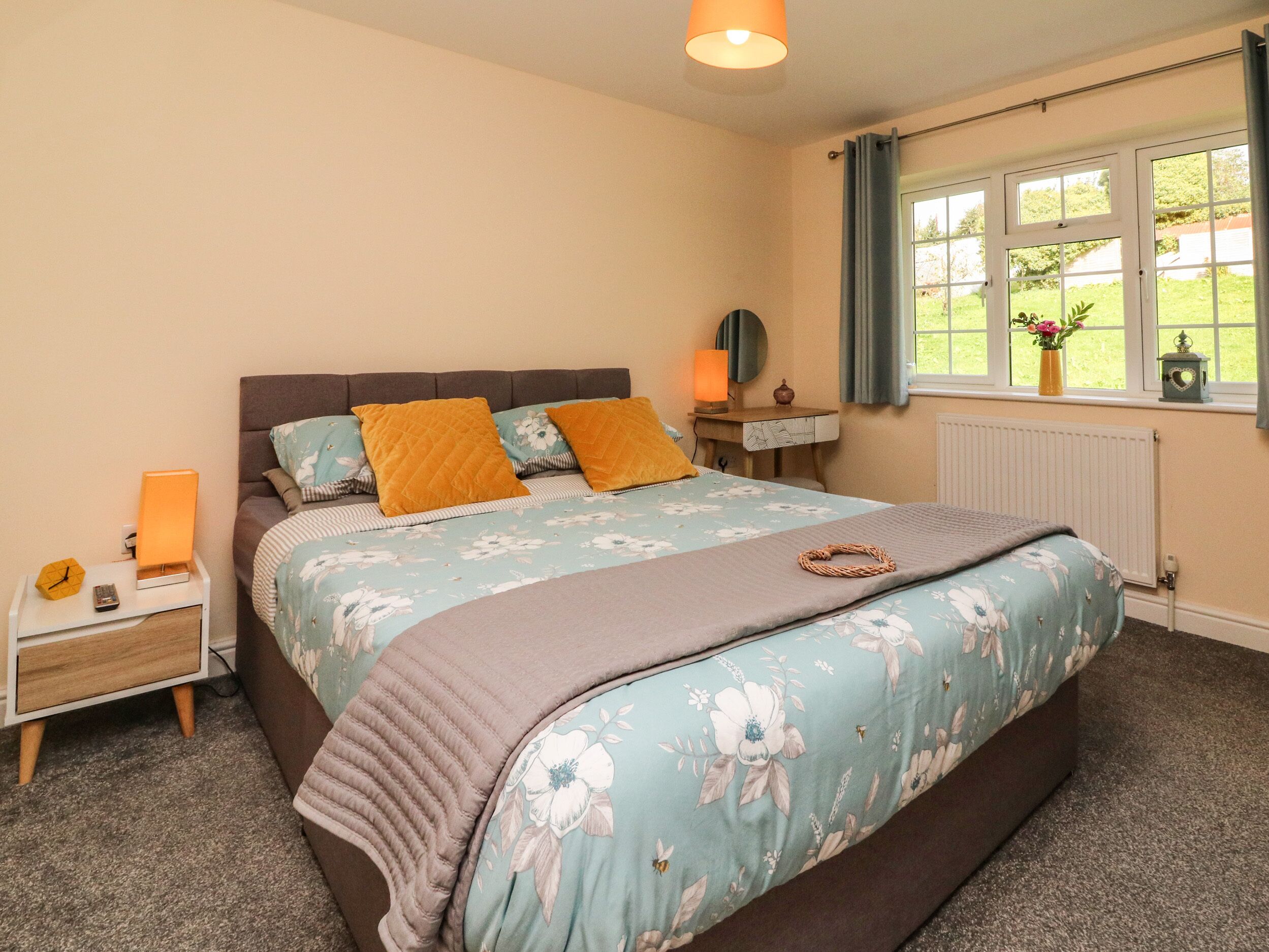 A bedroom with a bed, bedside tables, a lamp, a window with curtains, and a view of greenery outside.