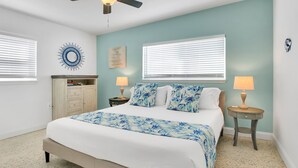 A bedroom with a bed, two bedside tables, a ceiling fan, and a wall-mounted circular decoration.