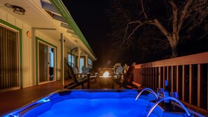 A hot tub with a wooden deck, a dining area with chairs, and a building with a porch. - Large recently remodeled home close to Yosemite.  Hot tub, EV, Game room. (Oakhurst)