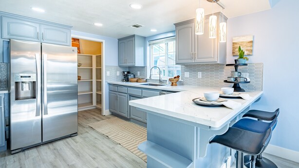 A modern kitchen with stainless steel appliances, a large island with bar stools, and a view of the backyard through an open door. - Large recently remodeled home close to Yosemite.  Hot tub, EV, Game room. (Oakhurst)
