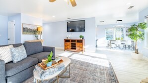 A living room with a gray sofa, a coffee table, a TV, and a dining area with a table and chairs. - Large recently remodeled home close to Yosemite.  Hot tub, EV, Game room. (Oakhurst)