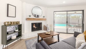 A modern living room with a fireplace, a sofa, a coffee table, and a view of a pool through large sliding glass doors.