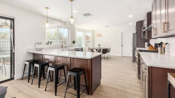 A modern kitchen with a central island, bar stools, pendant lighting, and stainless steel appliances.