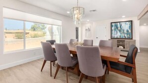 A modern dining room with a large wooden table, grey upholstered chairs, and a chandelier.