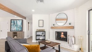 A modern living room with a gray sofa, a wooden coffee table, a fireplace, and a large TV.