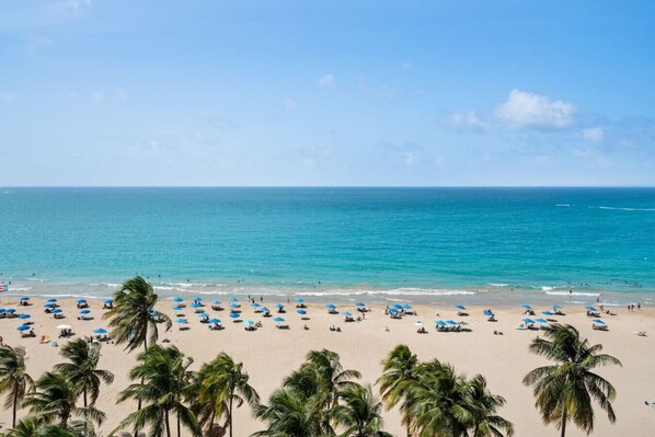 A beach with palm trees and blue umbrellas.