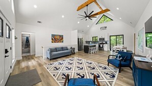 A spacious living area with a modern kitchen, a dining area, and a large window overlooking greenery. - Lake Loop Retreat w/Movie Theater & Private Dock (Speedwell)