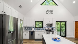 A modern kitchen with white cabinets, stainless steel appliances, a large island, and a view of the outdoors. - Lake Loop Retreat w/Movie Theater & Private Dock (Speedwell)