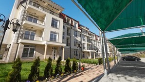 A multi-story residential building with balconies, a covered parking area, and a well-maintained garden.