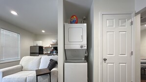 A compact living space with a kitchenette, a white sofa, a small table, and a door. - 1BR Near DT & Mountain Goat Cafe (Greenville)