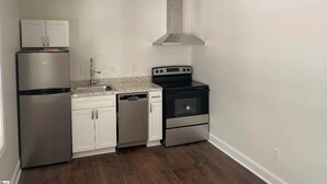 A compact kitchen with white cabinets, a stainless steel refrigerator, a dishwasher, a stove, and a range hood. - 1BR Near DT & Mountain Goat Cafe (Greenville)