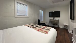 A bedroom with a bed, a desk, a chair, a TV, and a window with blinds. - 1BR Near DT & Mountain Goat Cafe (Greenville)